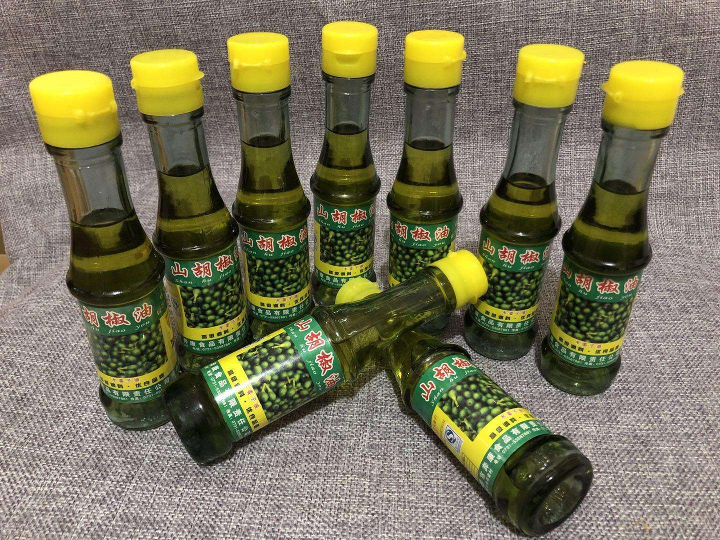 一组山胡椒衍生产品的陈列图,包括玻璃瓶装整粒山胡椒、研磨瓶装胡椒粉、棕色滴管精油瓶、独立小袋泡茶包以及印有‘高黎贡山野生’字样的礼盒包装,背景为木质展台与绿植装饰,整体风格偏向自然有机美学 山胡椒系列产品展示