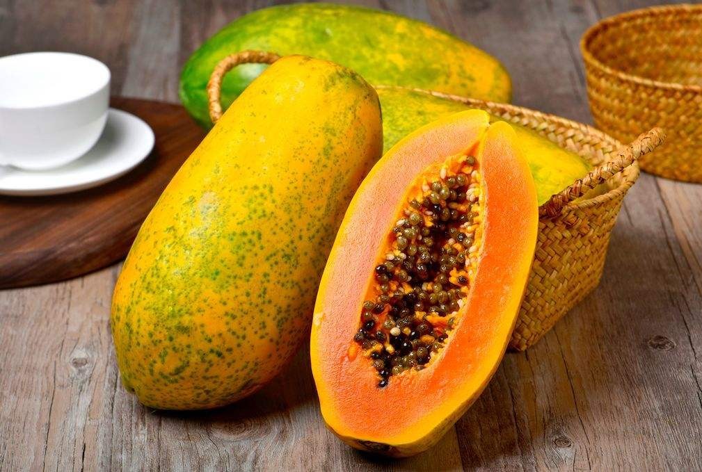 一个成熟的木瓜被纵向切开,露出橙红色的果肉和黑色的籽,果肉饱满多汁,背景为木质餐桌,自然光线照射,突出其新鲜与可食用性 木瓜切开特写