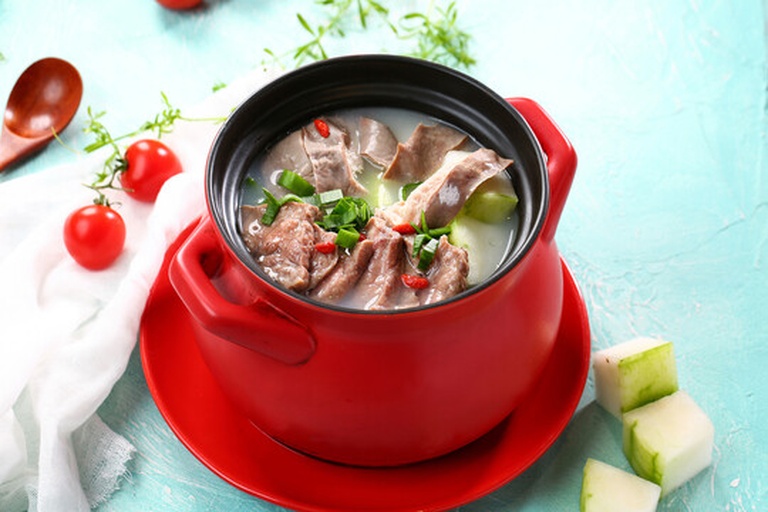 一口砂锅中正在炖煮乳白色汤汁的猪肚鸡汤,锅边可见拍裂的白胡椒粒和姜片,热气腾腾,背景为木质餐桌,营造温暖家庭氛围 猪肚鸡汤炖煮过程