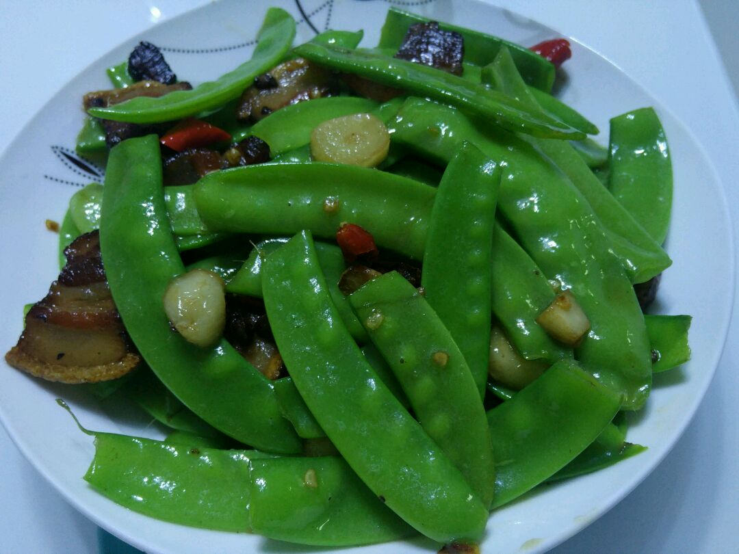 厨师正在用铲子翻炒锅中的荷兰豆与五花肉