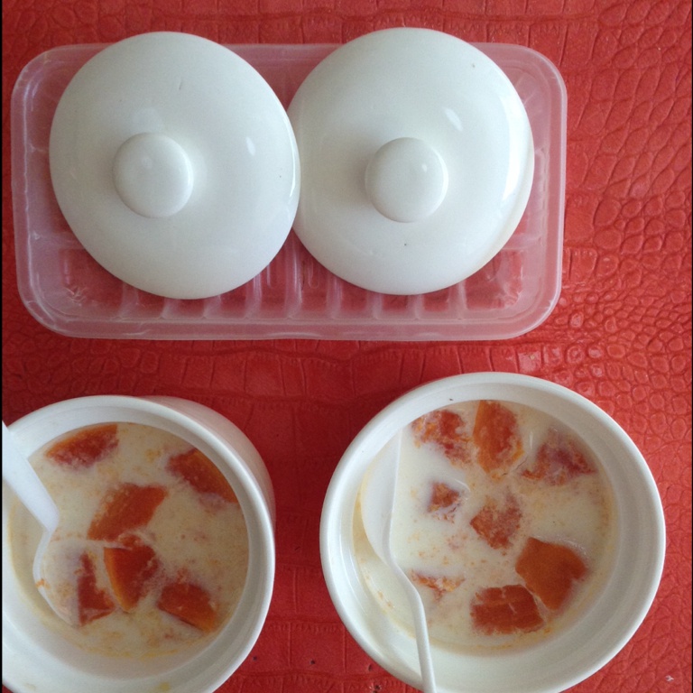 一个透明玻璃杯中分层呈现的木瓜椰奶冻,下层为乳白色椰奶冻,上层为淡橙色木瓜椰奶层,表面撒有白色椰丝和绿色薄荷叶,置于浅色餐巾布上 木瓜椰奶冻特写