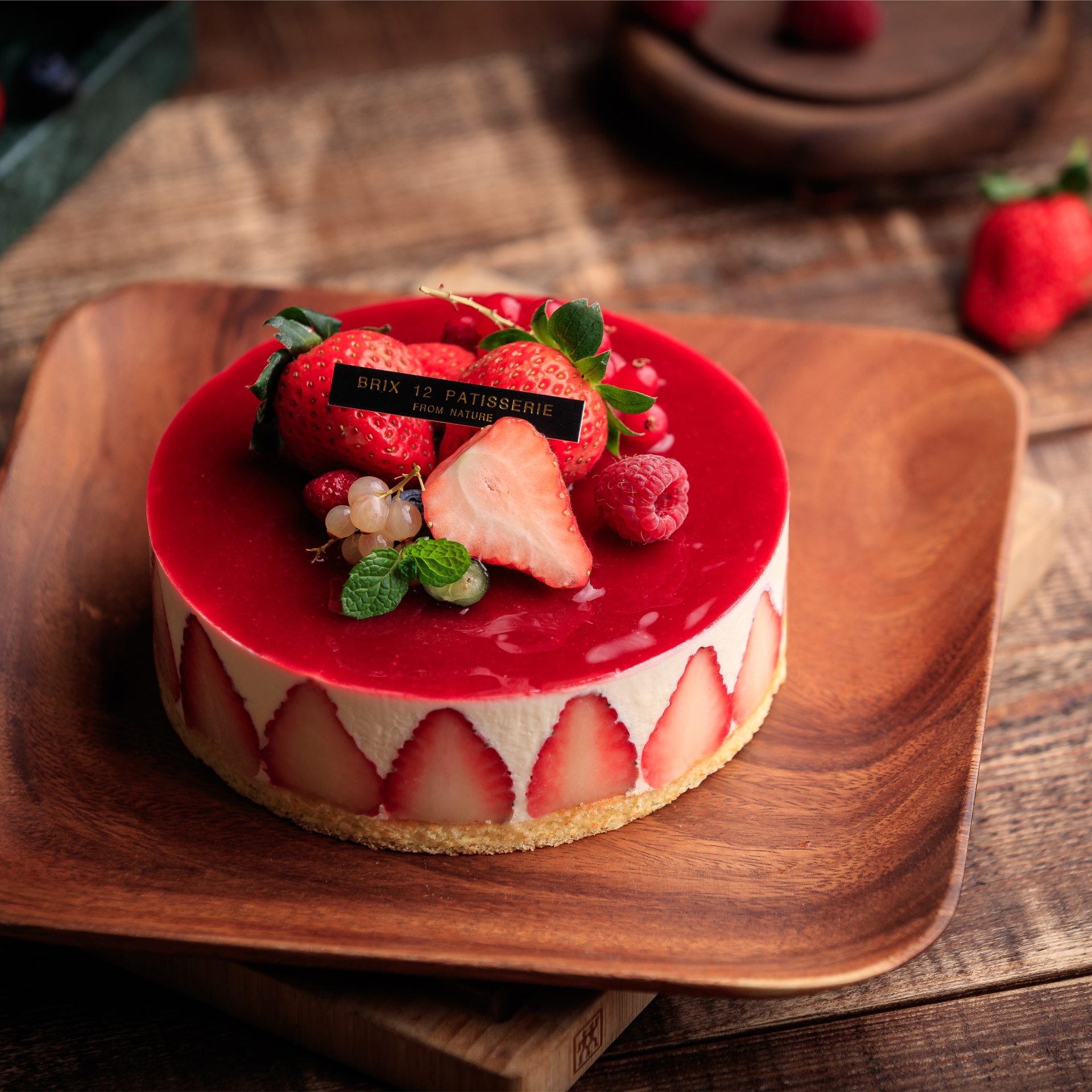一个透明玻璃碗中盛有粉红色的草莓慕斯糊,旁边摆放着泡软的吉利丁片、打发中的淡奶油和切好的草莓块。操作台上有序排列着量杯、搅拌碗、刮刀和6寸慕斯模具,背景为现代厨房,灯光柔和 草莓慕斯组装与冷藏过程