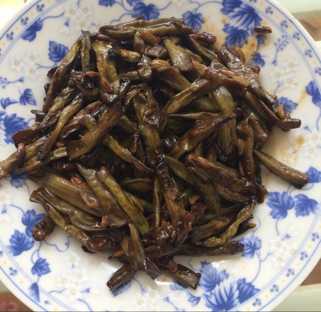 干煸四季豆成品特写：深翠带褐斑的四季豆整齐铺于白瓷盘中，表面油润不泛光，可见清晰虎皮纹路，点缀金黄蒜末、焦红辣椒段与青翠葱花，背景虚化木质餐桌