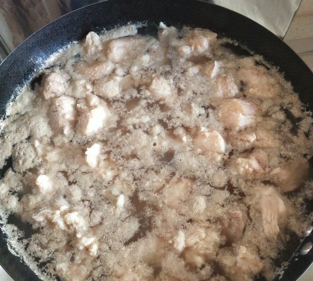 一只深色陶锅中正在煮沸的鸭肉块,水面漂浮着灰色浮沫,旁边摆放着切好的姜片和一瓶料酒,背景为厨房操作台,光线柔和自然 鸭肉焯水过程