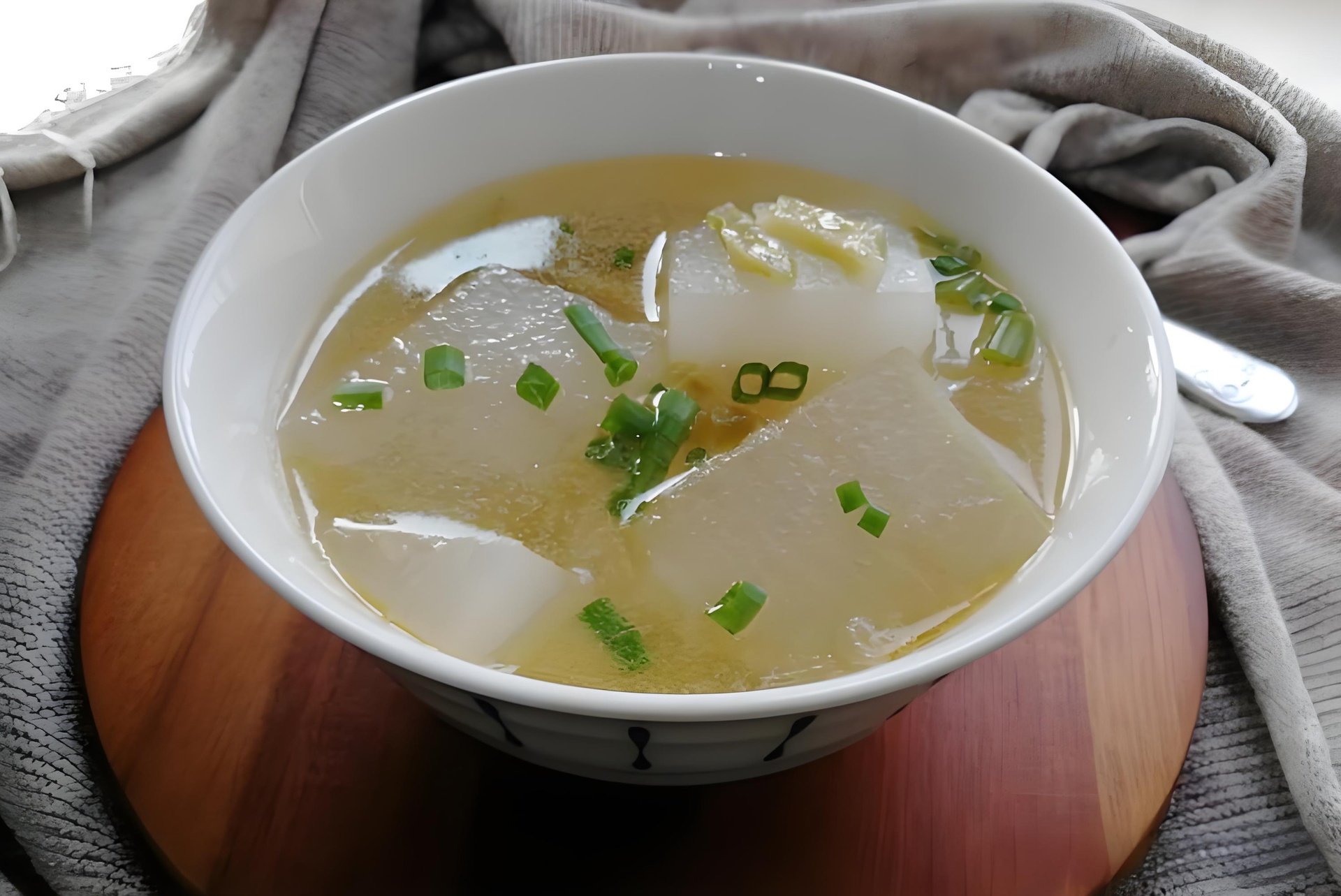 一碗刚出锅的水果萝卜炖汤特写,汤体清澈略带乳白,萝卜块呈半透明状,枸杞点缀其间,上方撒有绿色葱花,展现诱人的食欲感 成品水果萝卜炖汤盛在白色瓷碗中,汤色清亮微白,萝卜块晶莹,点缀枸杞和葱花