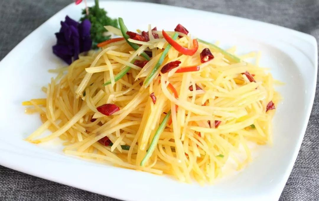 一张餐桌上摆放着多道家常菜，中央是一盘色泽诱人的尖椒土豆丝，周围有米饭、汤碗和筷子，营造出一家人围坐吃饭的温馨场景