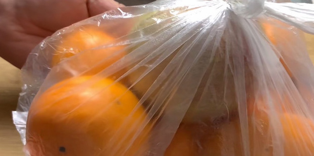 透明塑料密封袋内装有两个橙红色脆柿和一个红富士苹果,袋子半扎口,放置在浅色木桌上,背景虚化,突出果实新鲜状态 脆柿与苹果共存催熟场景