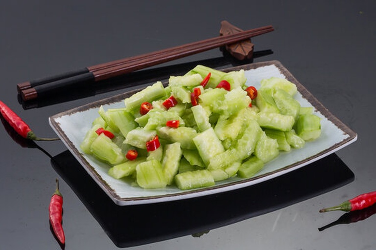 一位穿着围裙的手正在使用黑色筷子搅拌一大碗刚拌好的菠菜黄瓜凉菜,碗中绿色菠菜与浅绿黄瓜交错分布,表面可见蒜末与红辣椒段,整体色泽清新诱人,背景为厨房台面 厨师正在一个白色瓷碗中用筷子搅拌菠菜和黄瓜,菜肴颜色鲜亮,黄瓜呈斜切片状,菠菜翠绿,表面有光泽