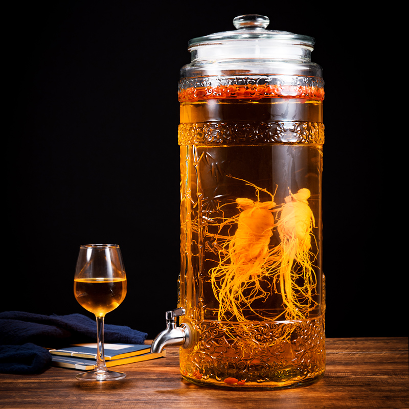 一位中年男性正在厨房内将一支洗净的人参放入玻璃瓶中，旁边放着一瓶 opened 的白酒