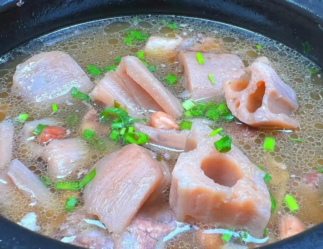 一口砂锅中正炖煮着莲藕与排骨,汤色呈乳白色,藕块清晰可见,表面微泛光泽,旁边摆放着葱段、姜片和调味料,整体画面温暖温馨,展现家常美食的治愈感 厨房中正在烹饪的莲藕排骨汤
