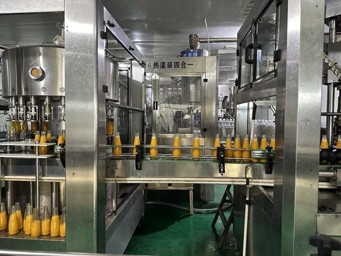 现代化NFC果汁生产车间内景,展示透明玻璃后的全自动榨汁、杀菌、灌装流水线,工人在控制屏前操作,地面洁净无尘,设备标注‘UHT瞬时灭菌’‘无菌冷灌装’字样 柑桔NFC果汁自动化生产线