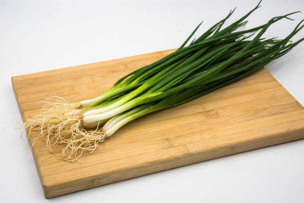 一个明亮的家庭厨房场景,木桌上摆放着一束刚买回的新鲜小葱,旁边有一把不锈钢剪刀和一个白色瓷盘,小葱根部湿润,叶片翠绿有光泽,体现其新鲜度和生活化使用场景 家庭厨房中新鲜小葱的摆放场景