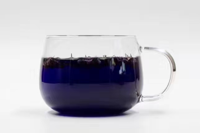 一杯透明玻璃杯中的果茶,内含浸泡过的脆柿切片、枸杞和茶叶,液体呈琥珀色,杯口有水汽升腾,背景为厨房窗台,窗外是秋天的树叶 脆柿制作的果茶饮品