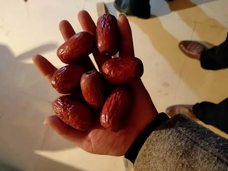 一位中年男性坐在餐桌旁,左手拿着血糖仪,右手手指正准备采血;桌上有一盘刚吃完的餐食,包含半根水果玉米、蔬菜和鱼肉,旁边放着记录本和笔,背景温馨居家 血糖监测场景图