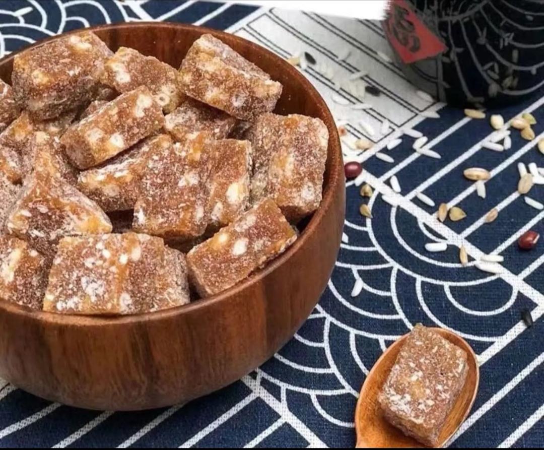 三排不同颜色和形态的姜母糖摆放在白色瓷盘上:左侧为深褐色传统红糖姜母糖块,中间为浅金黄色蜂蜜姜母糖,右侧为乳白色的奶香姜母糖,背景为木纹桌面与一小束干尤加利叶装饰 不同口味姜母糖成品展示