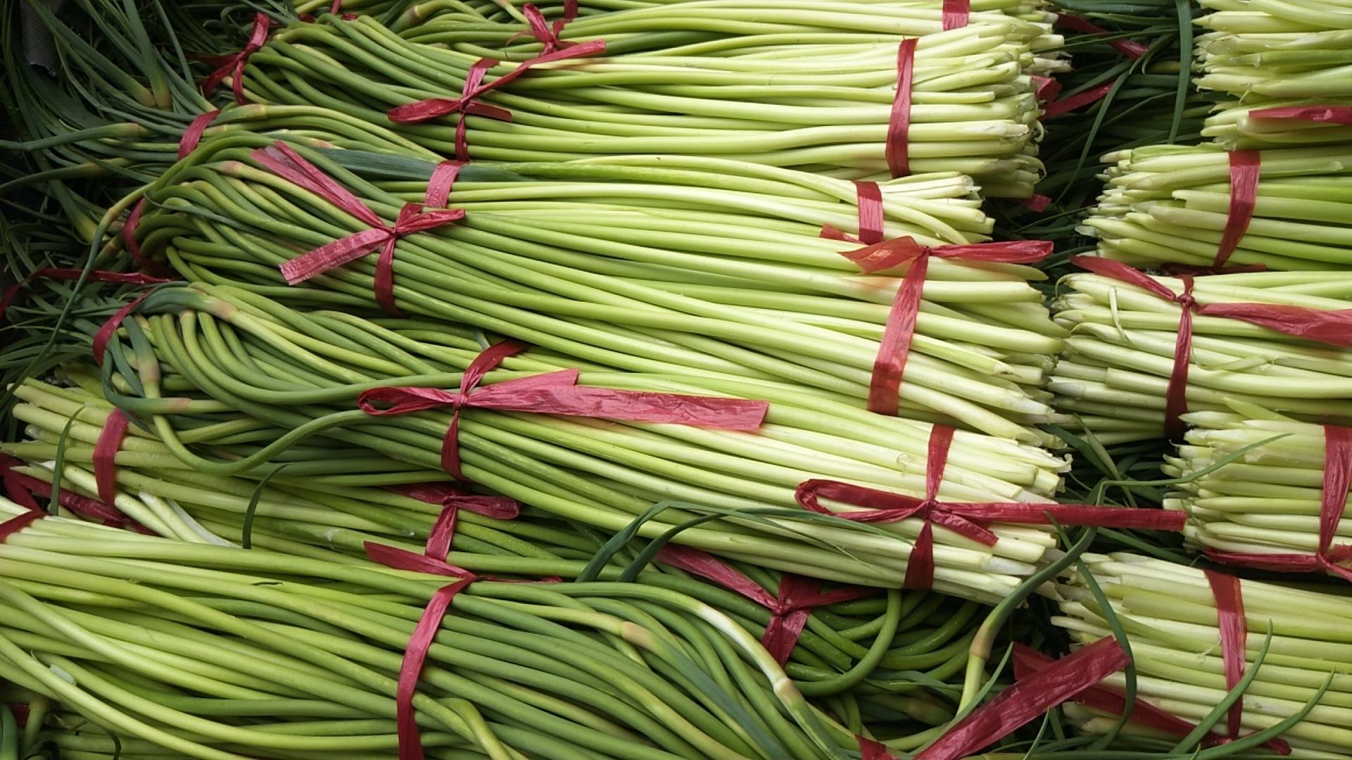 新鲜翠绿的蒜薹,带有微微紫红色边缘,摆放在竹篮中 新鲜蒜薹特写