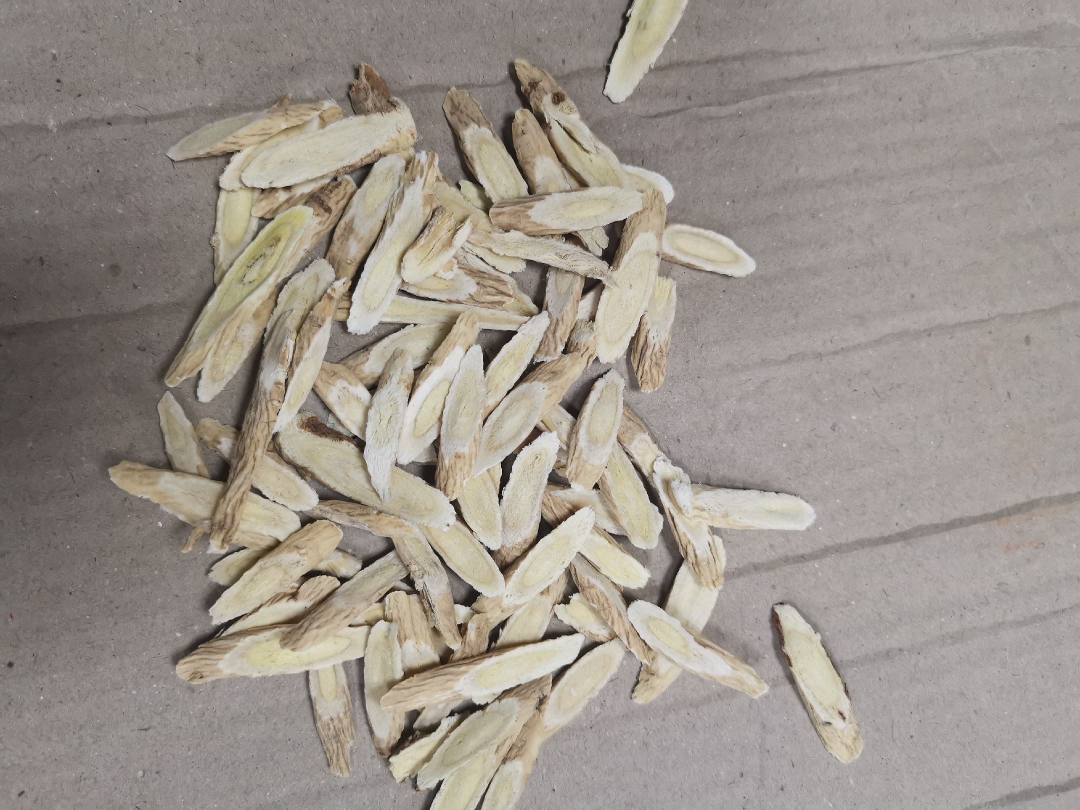 中药师手持电子天平称量黄芪饮片特写：天平显示屏清晰显示"20.0g"，托盘中整齐铺放21片完整黄芪切片，背景为木质操作台与中药斗柜虚化