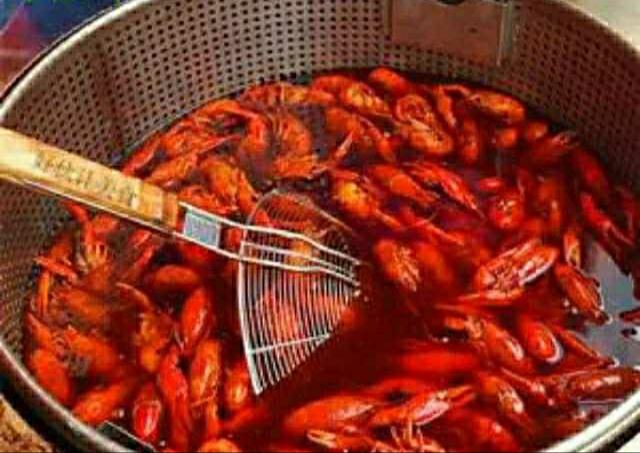 一家烟火气浓郁的街边麻辣小龙虾大排档实景，蓝色遮阳棚下摆着七八张折叠圆桌，穿围裙的老板正手持长筷翻炒铁锅中的红亮小龙虾，锅气升腾，旁边不锈钢盆里堆满待加工的青壳活虾，地面干净无油污，体现市井但规范的经营状态