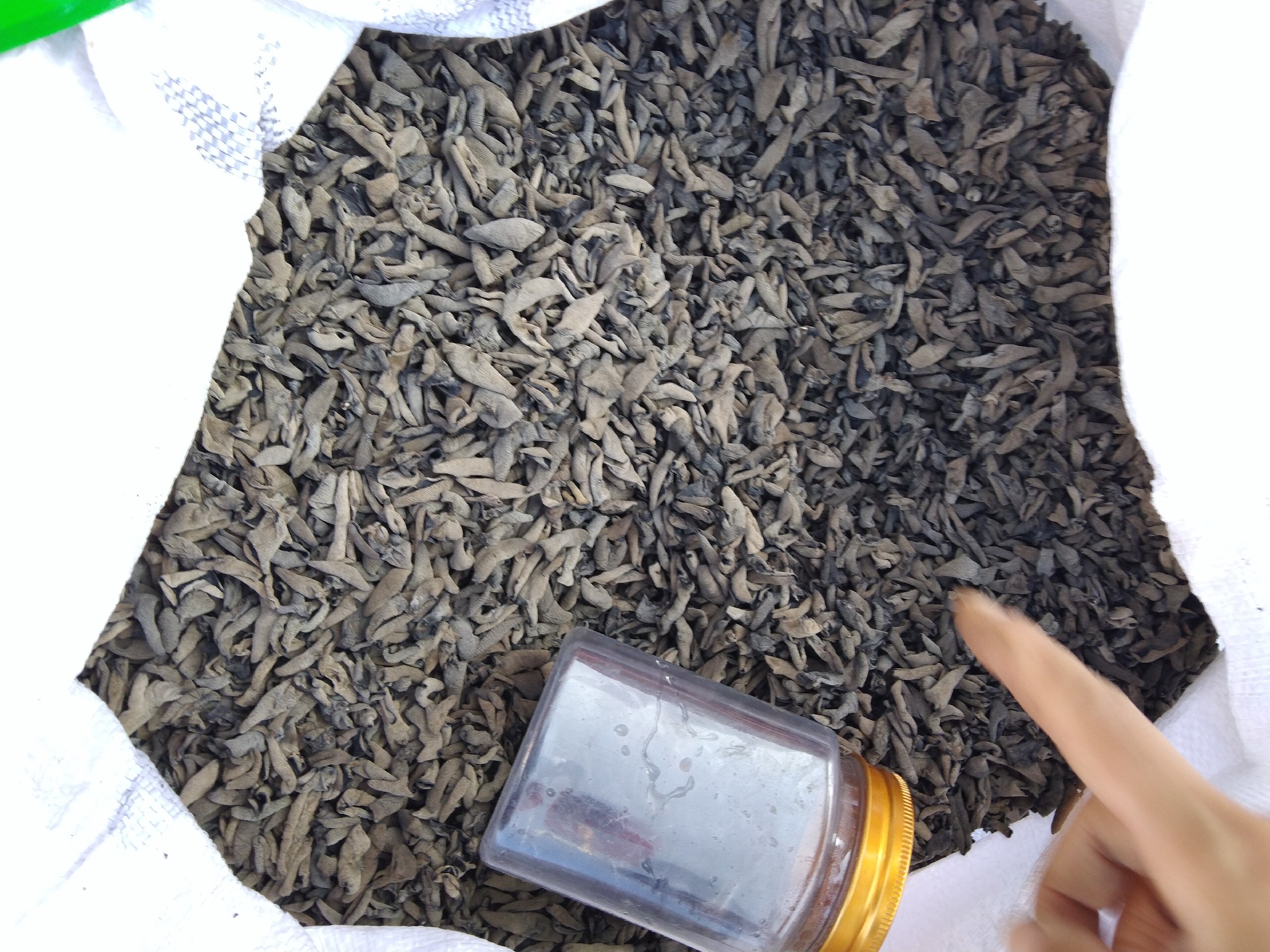 一个透明玻璃密封罐中装有干燥的黑木耳,放置在整洁的厨房操作台上;旁边是一包未拆封的原装黑木耳,标签上显示生产日期和保质期;背景中有调味瓶、砧板等厨具,整体环境干净明亮 家庭厨房中干黑木耳的储存场景