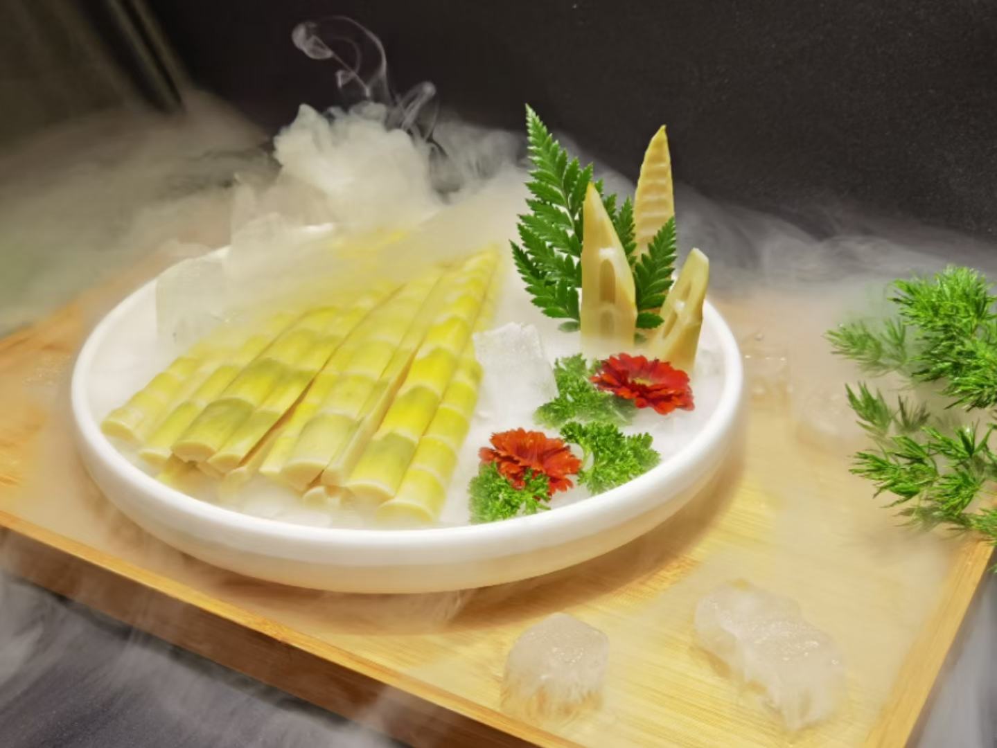 一张木质餐桌上摆放着两个白色瓷盘,一个盘中是切开的山竹,露出洁白的蒜瓣状果肉;另一个盘中是洗净切段的山芹,颜色翠绿,带有细长叶片。旁边有一杯清水和一把小勺,整体呈现清新自然的饮食风格 山芹与山竹并置的餐桌摆盘