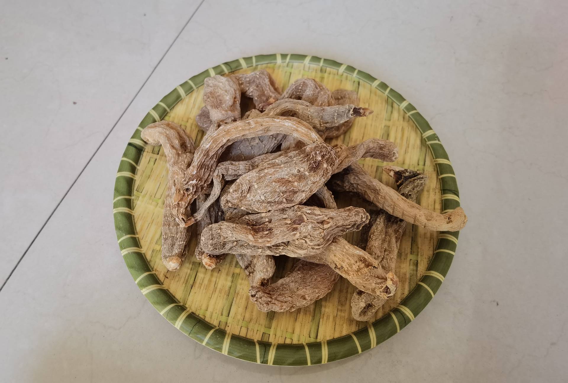 一个传统中药材交易市场的木质柜台,摆放着多个竹编簸箕,分别盛放天麻整块与切片、白芷原根与饮片,背景可见‘正宗昭通天麻’‘道地禹白芷’的手写招牌,光线柔和,体现真实交易环境 中药材市场摊位实景图