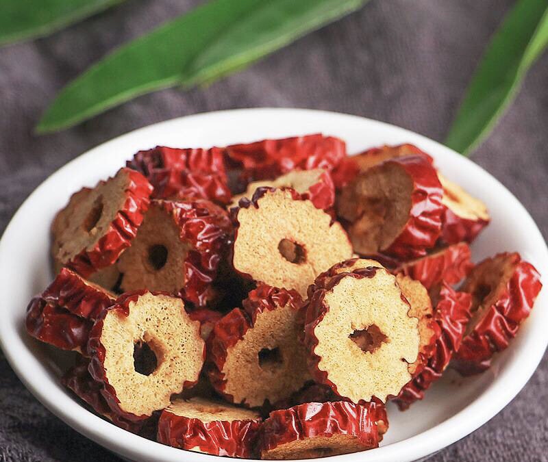 一盘浅褐色的干红枣片平铺在白色陶瓷碟中,背景为柔和自然光下的厨房台面,红枣片边缘微卷,表面有自然褶皱和光泽,部分可见果核残留,整体呈现干燥但不失润泽的状态 干红枣片特写