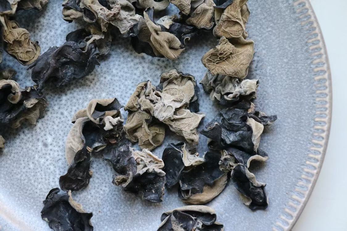 左侧为一小堆干燥的黑木耳干品,深黑色,卷曲状;右侧为同一份木耳经冷水泡发6小时后的状态,体积膨大数倍,呈半透明胶质状,铺展在白色瓷盘中 黑木耳泡发前后对比图