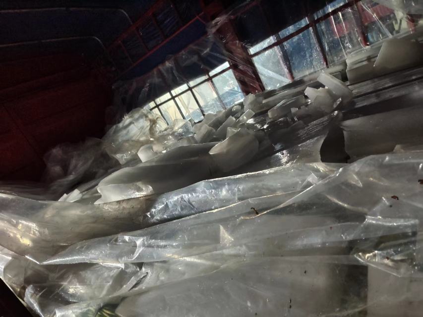 中国北方某大型蔬菜批发市场蒜薹交易区实景：多辆冷链货车上卸下成捆蒜薹，批发商手持电子秤称重，纸箱印有“山东金乡·一级蒜薹”字样，现场悬挂“严禁使用‘蒜苔’等不规范品名”提示牌