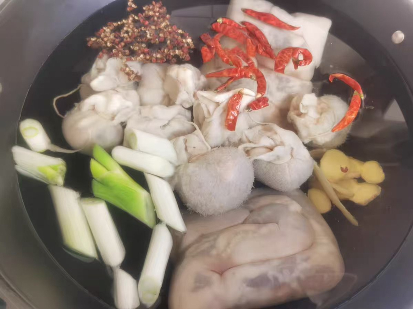 展示羊肉在锅中焯水的过程,锅内有白色泡沫,旁边摆放着生姜和料酒 羊肉焯水过程