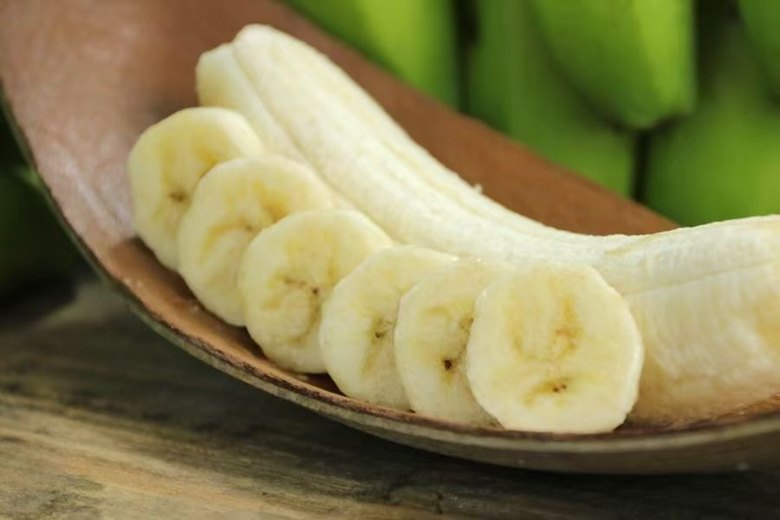 一盘切好的香蕉片摆放在木质餐盘中，背景为自然光线下的厨房环境，旁边放有标注“600g”的标签纸