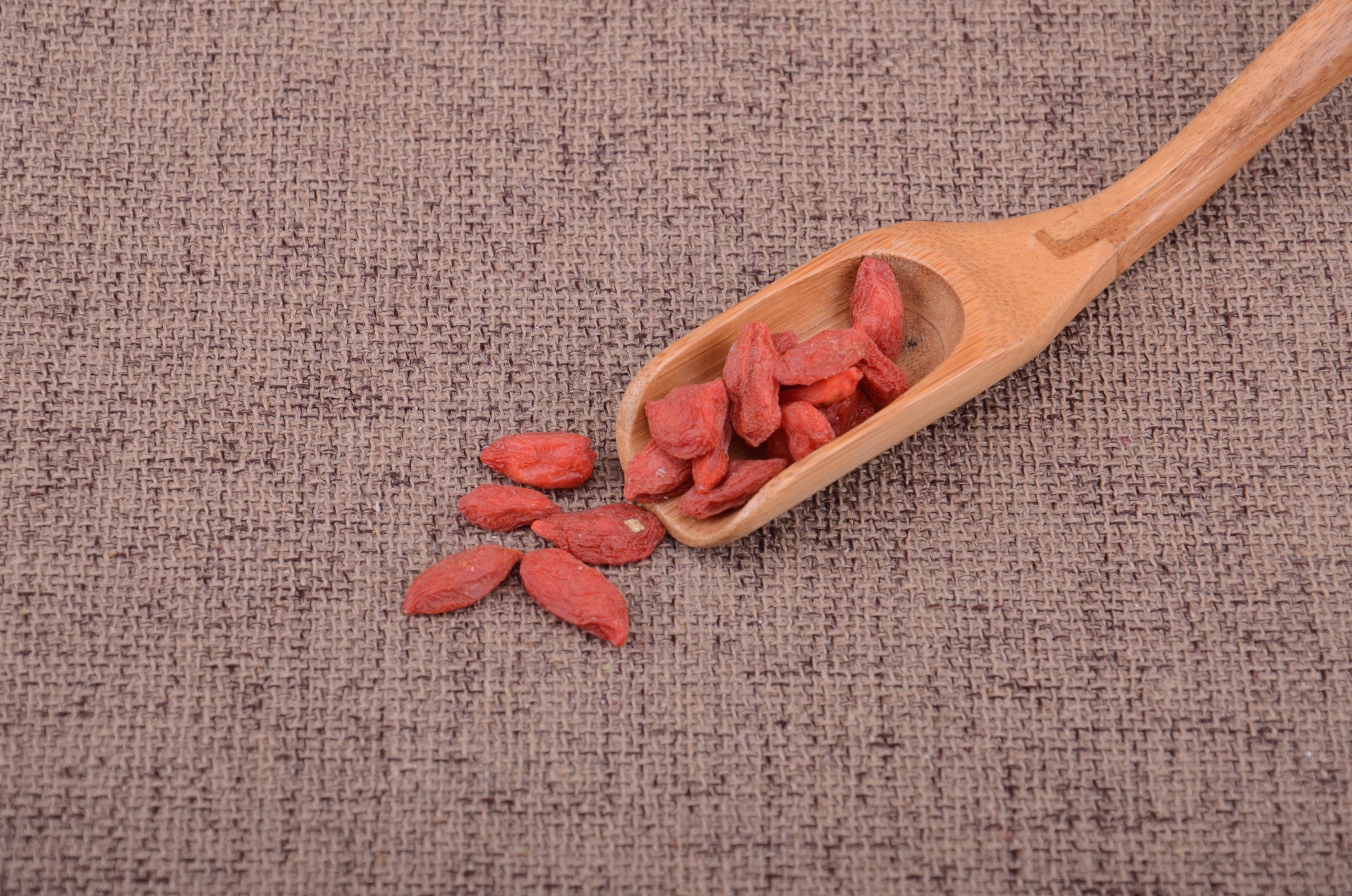 桌面上摆放着一小堆红色枸杞,旁边放置电子秤显示20克读数,另有一把不锈钢勺子和两个塑料瓶盖,用于直观展示枸杞与常用容器的关系 枸杞与量具对比图