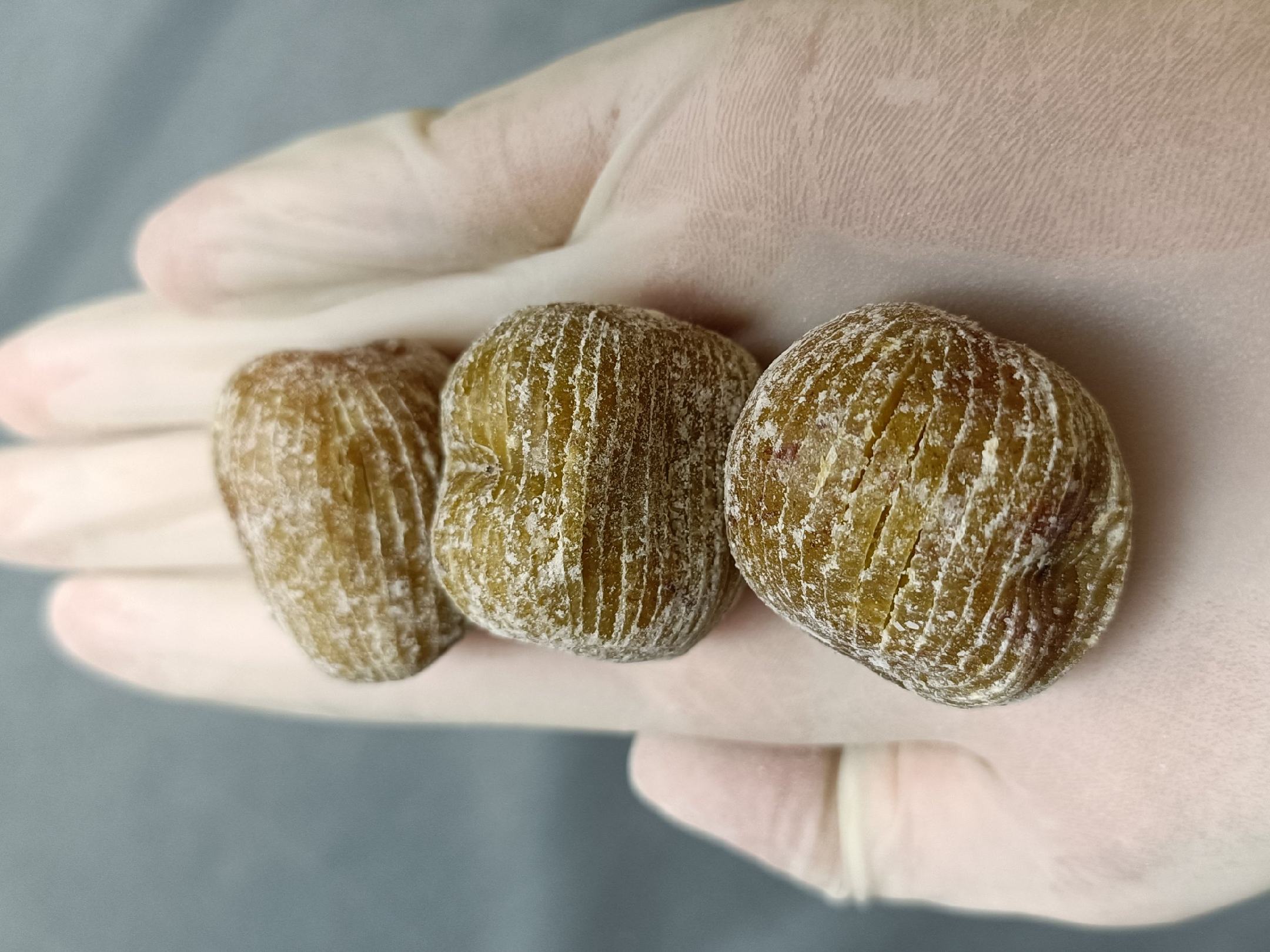 一只手戴着食品级乳胶手套,在透明玻璃碗中轻轻揉搓干红枣片与淡黄色粉末的混合物,旁边摆放小勺和三个调料瓶,标签清晰可见:蜂蜜粉、柠檬粉、苏打粉 红枣片调味混合过程