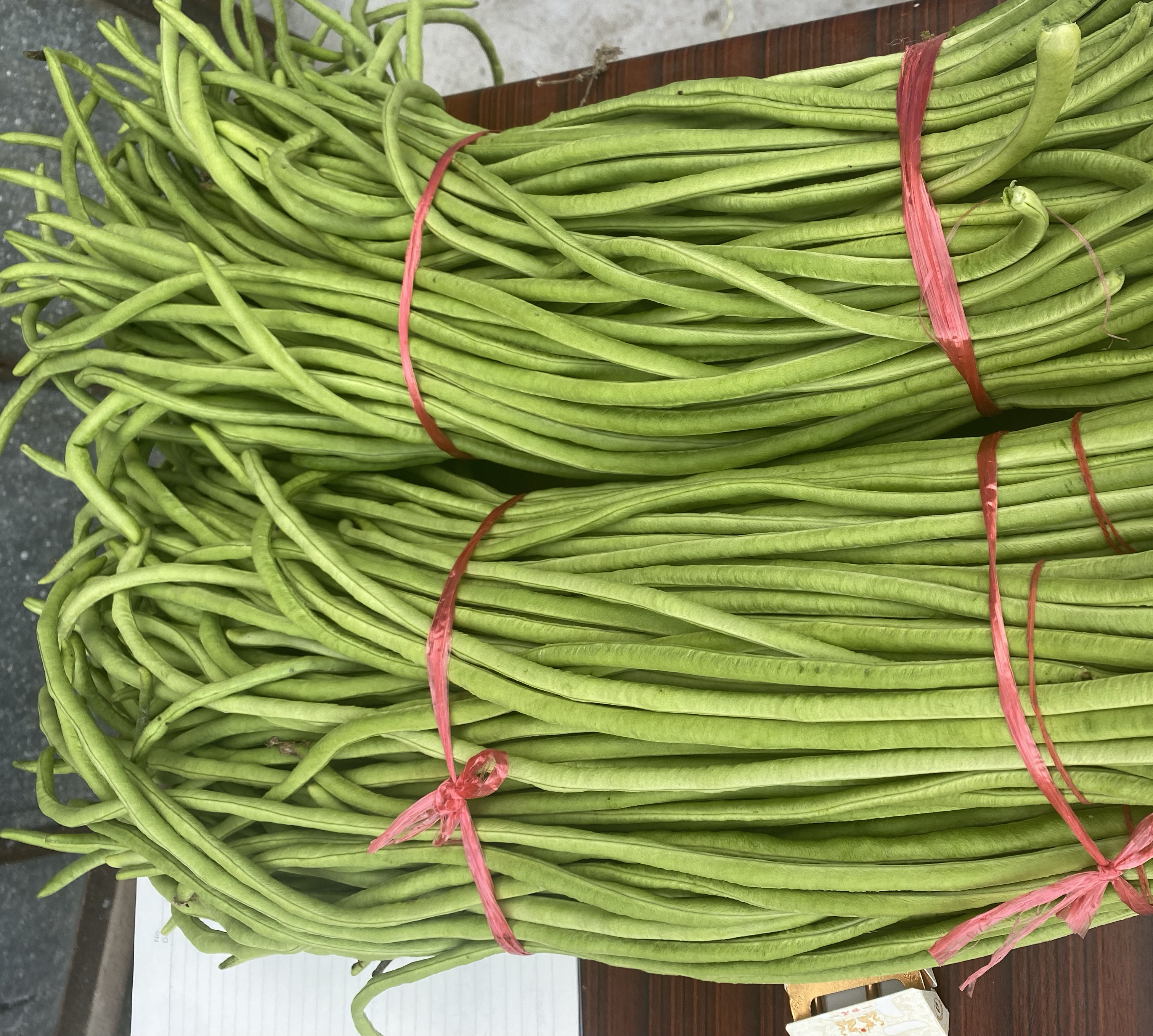 高清微距图:左手固定青绿色豆角段,右手拇指与食指捏住豆角一侧边缘,沿纵向轻巧撕下一条半透明浅褐色筋膜;豆角表皮完整无破损,切口整齐呈45°斜角 豆角去筋操作特写