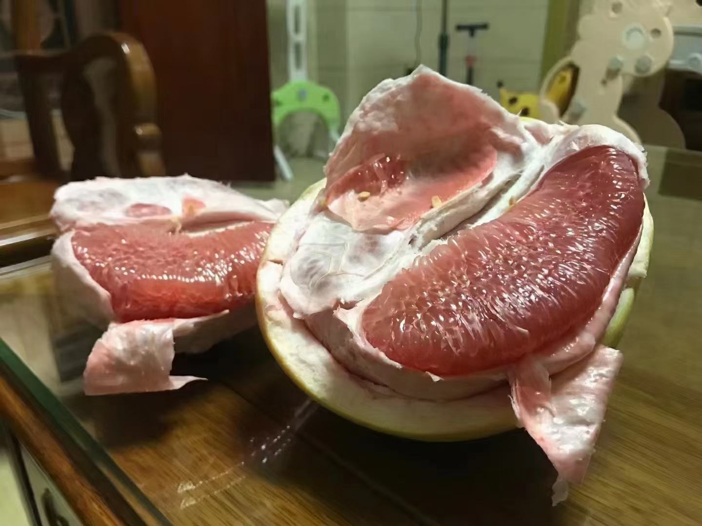 一个成熟的沙田柚红肉品种被横向切开,露出鲜艳的粉红色果肉,果瓣饱满分明,汁水丰富,表面有晶莹光泽,背景为田园果园环境,阳光柔和 沙田柚红肉切开特写