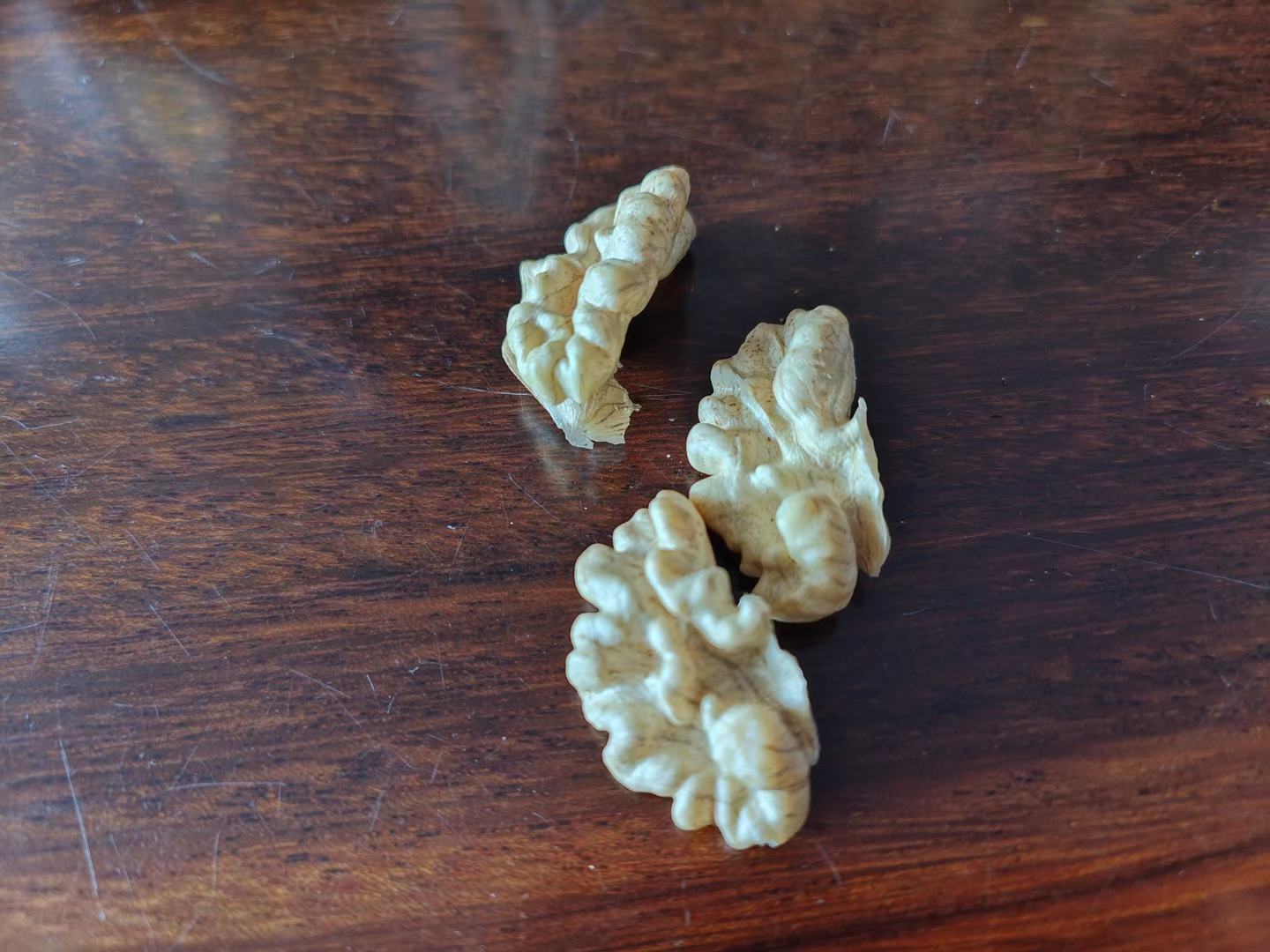 一名消费者正在桌面上对比三种不同的核桃样品:左侧为自然色纸皮核桃,中间为疑似漂白过的雪白核桃,右侧为普通厚壳核桃;旁边放有一杯清水用于泡水测试,桌上还有一张pH试纸 消费者对比不同核桃样品