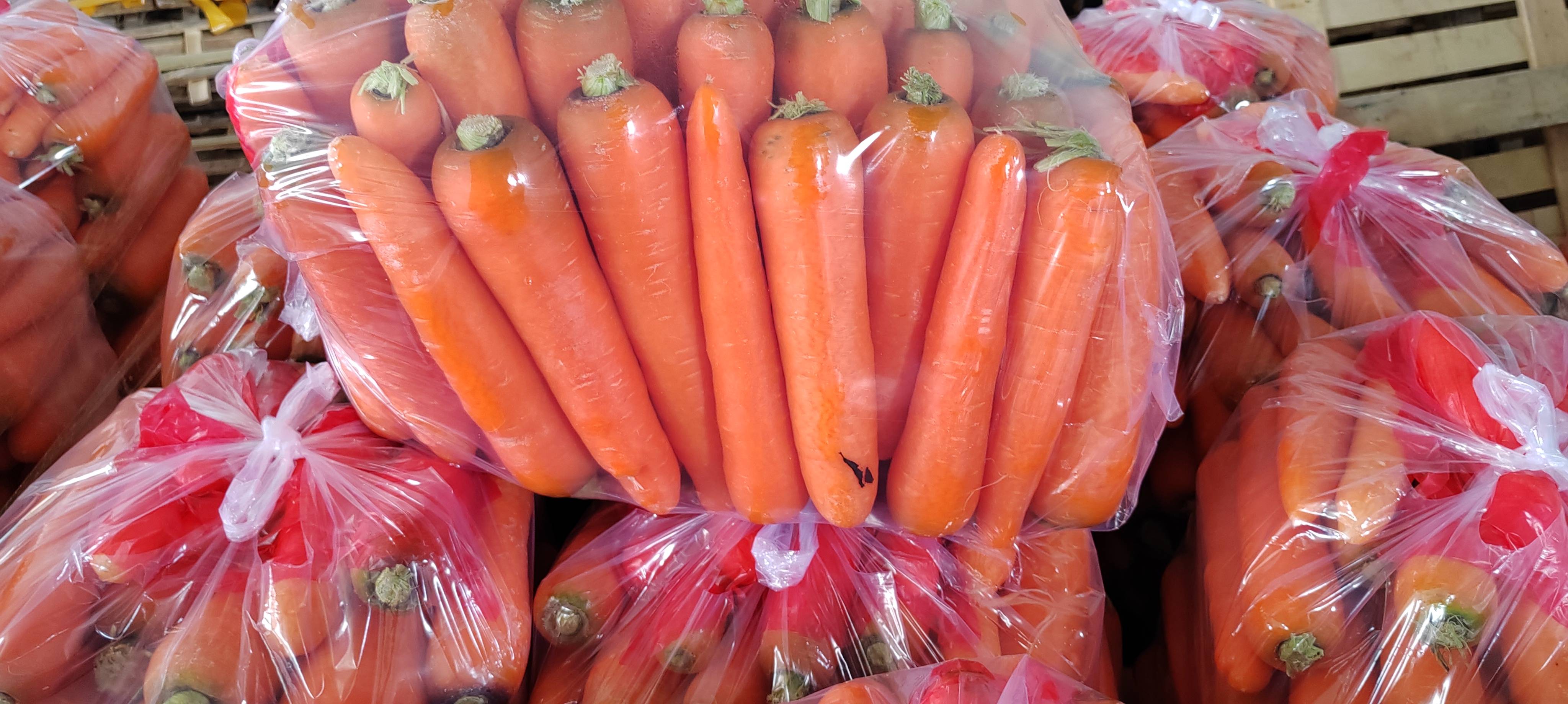 展示一篮新鲜橙红色胡萝卜,背景为农田或市场环境 新鲜胡萝卜展示图