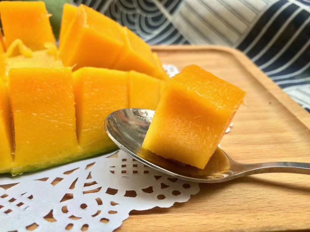 图片展示大青芒制作的美食拼盘,包括芒果奶昔、芒果沙拉和芒果班戟,背景为厨房操作台,突出美食与水果的搭配美感 大青芒美食拼盘