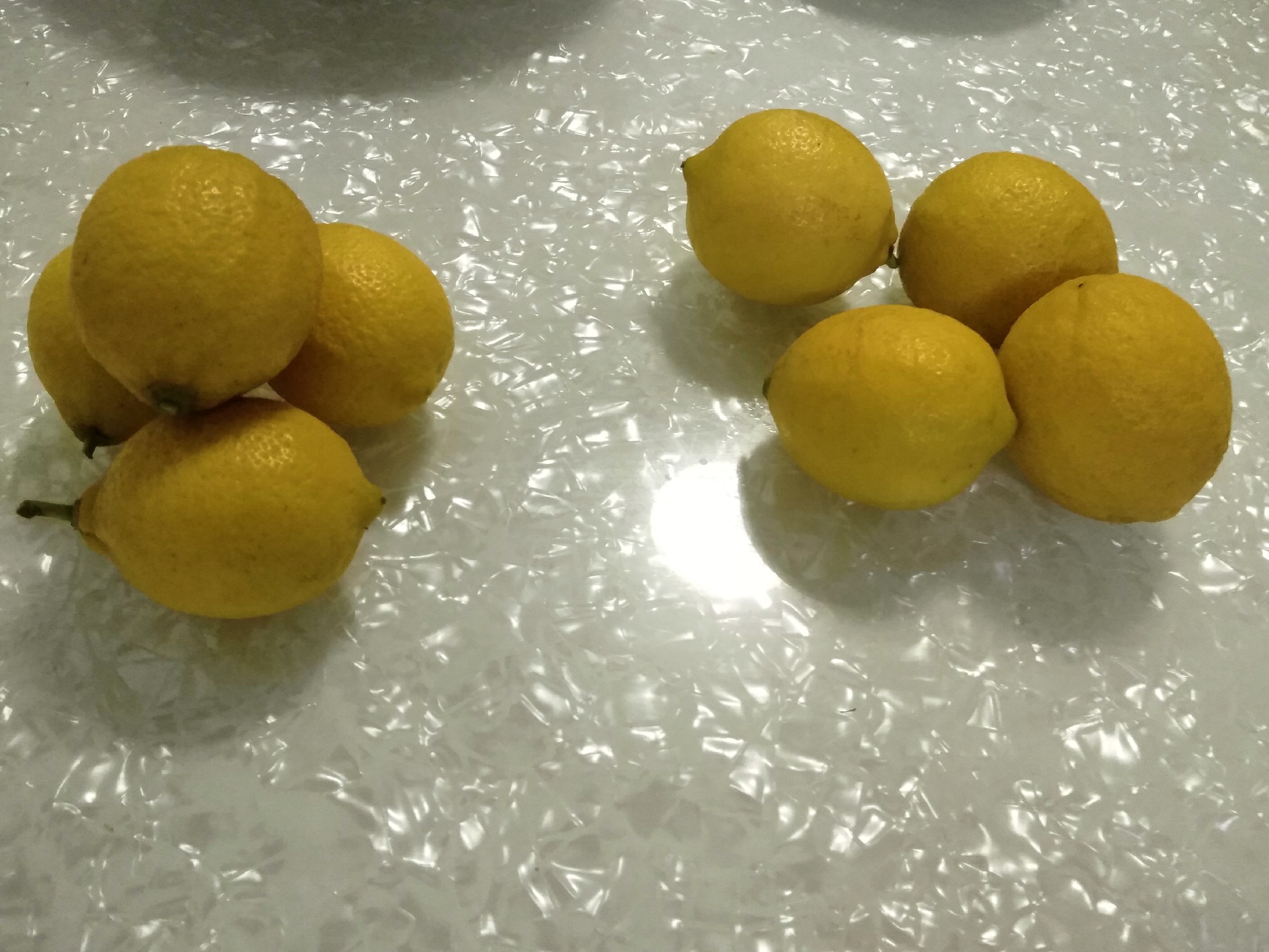 玻璃杯中浸泡着两片金黄色的柠檬干,热水冲泡后颜色渐变为浅琥珀色,气泡缓缓上升,旁边摆放一碟完整的柠檬干片和半个新鲜安岳柠檬,背景虚化呈现厨房台面 柠檬干泡水过程特写