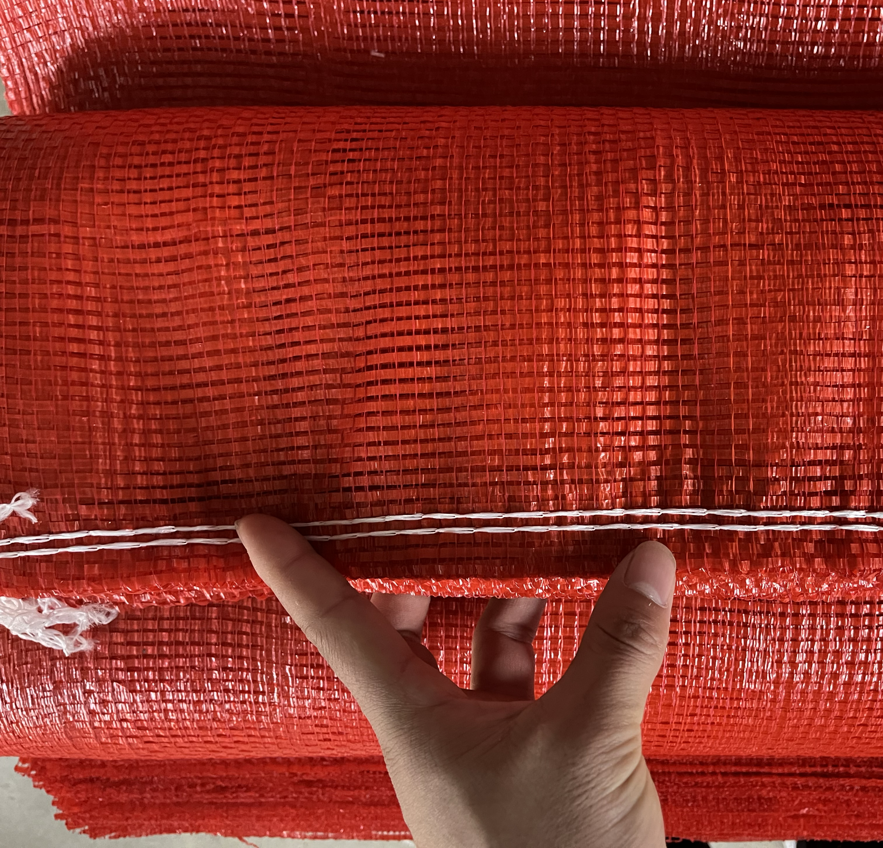 身穿工作服的仓库人员正在打开网袋检查洋葱状态,手持记录本和手电筒,专注查看洋葱是否出现发芽或腐烂现象,背景为成排堆放的洋葱袋,体现日常维护管理场景 工人正在检查储存中的洋葱质量
