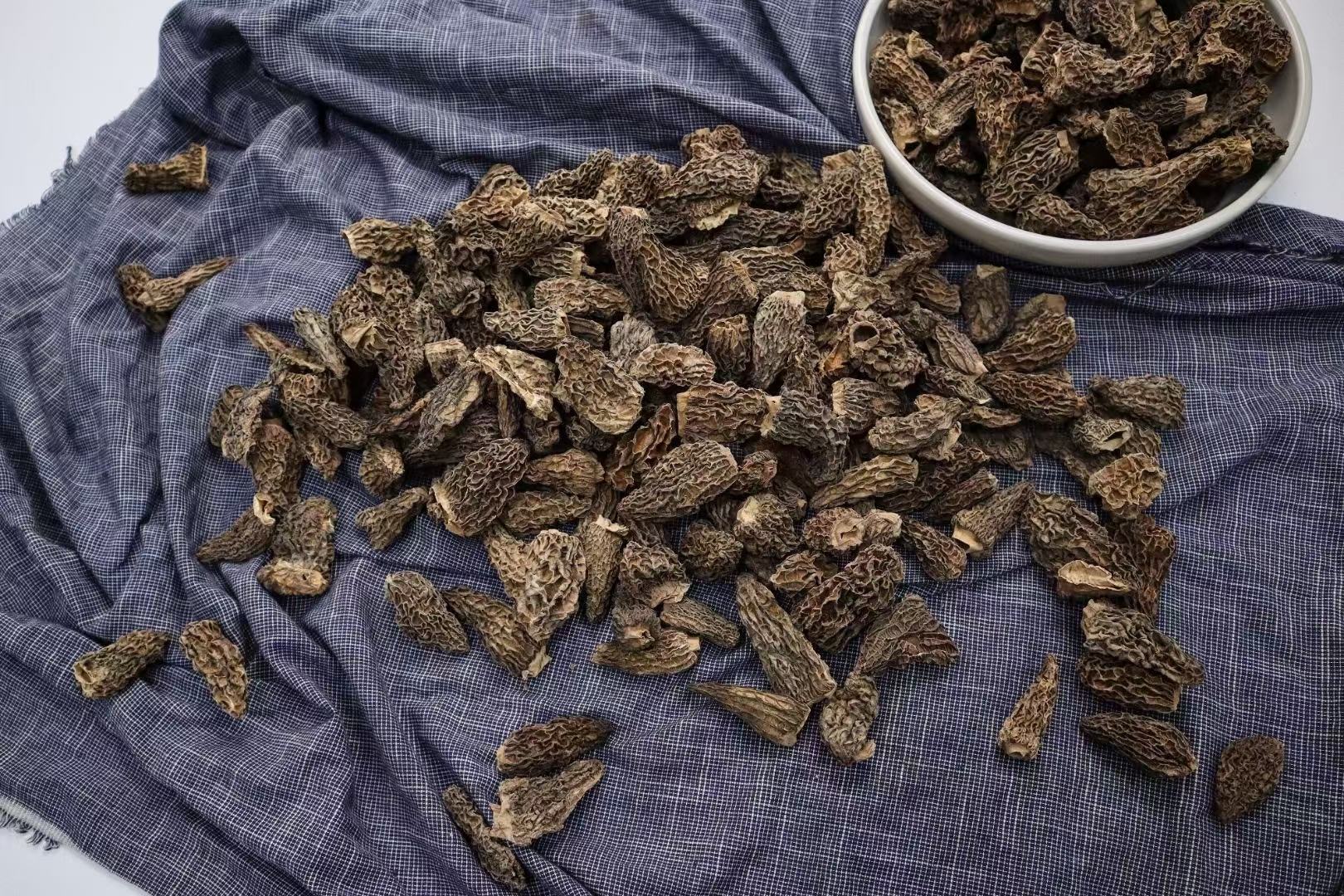玻璃托盘中整齐排列的干制羊肚菌,分为四组:特级(最大)、一级、二级、统货,配有标签说明尺寸范围和产地信息,背景为木质餐桌,体现高品质食材陈列 羊肚菌干品分级展示图