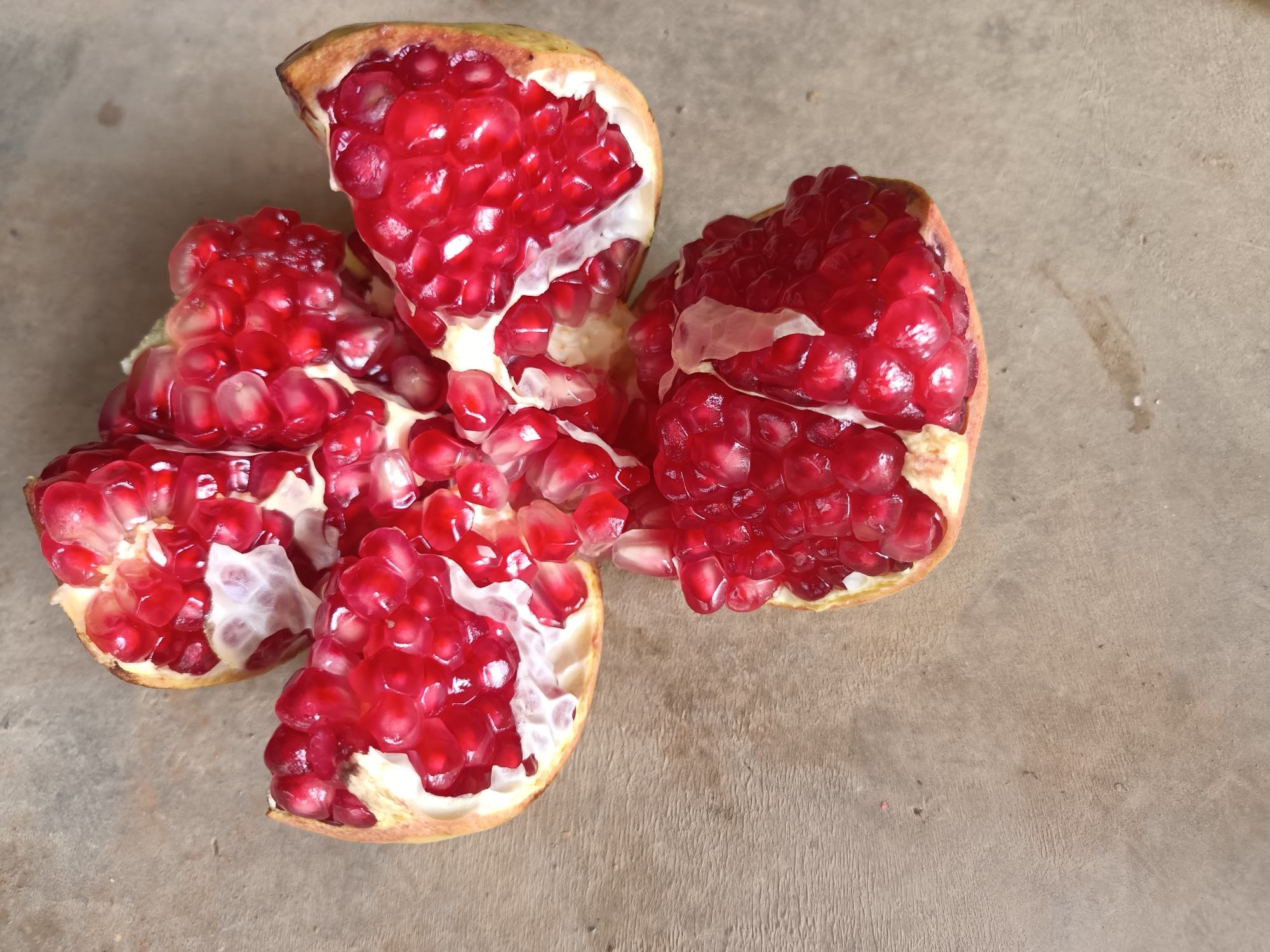 一个被横向切开的突尼斯软籽石榴,露出内部晶莹剔透的红色籽粒,排列整齐密集,汁水充盈,旁边放置一把不锈钢勺子以便对比大小,背景为白色陶瓷盘和木制餐桌,突出食材的新鲜与居家食用场景 软籽石榴切开展示内部结构