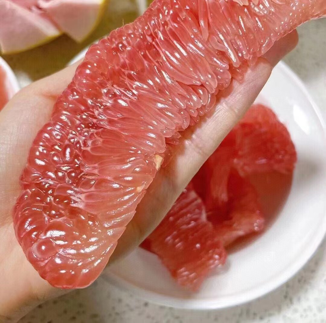 一个新鲜的柚子被切开,露出晶莹剔透的果肉,果瓣分明,果汁丰富,展示出柚子的自然美味 新鲜柚子切开图