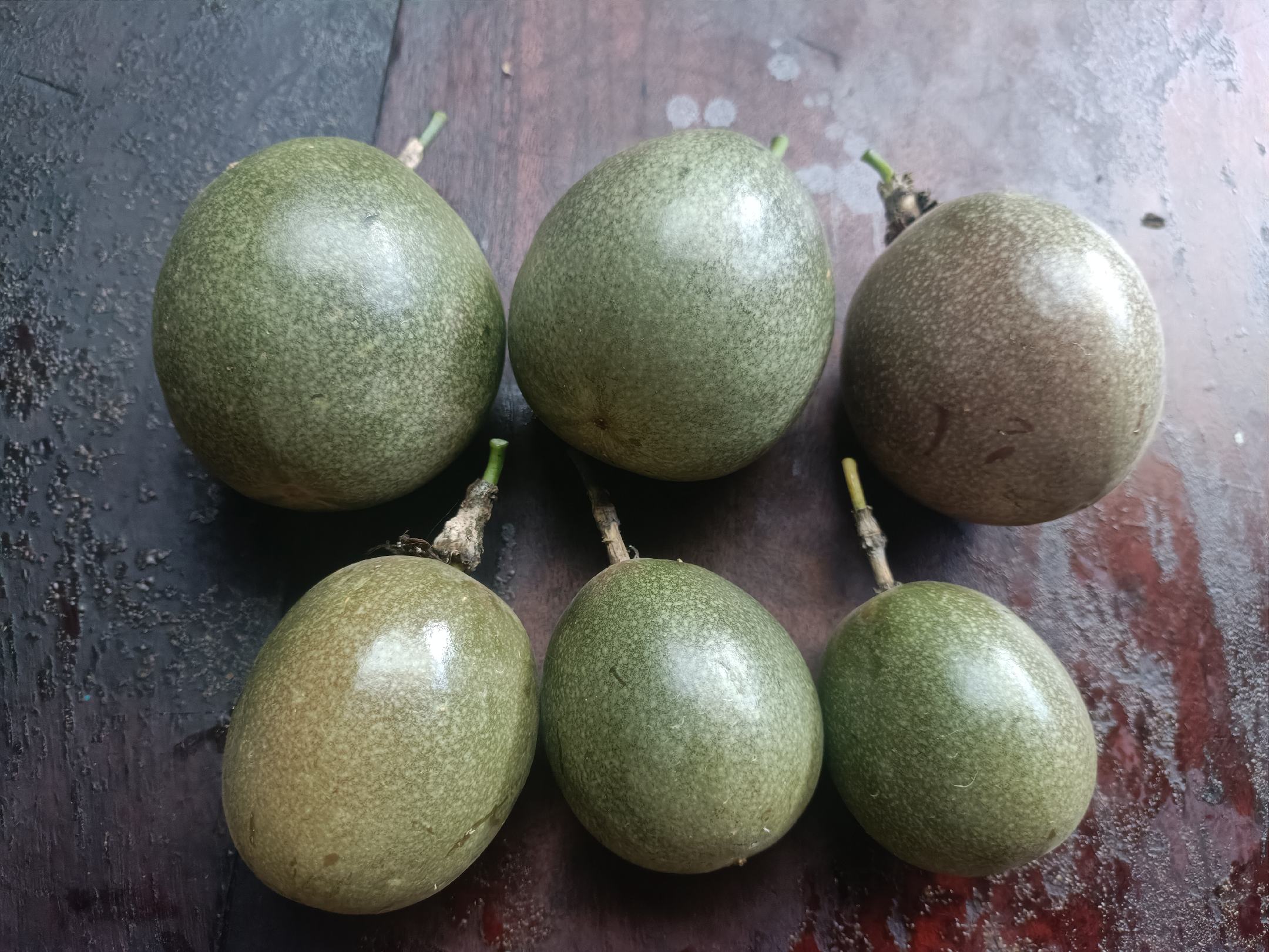 一张木制餐桌上的牛皮纸袋微微打开,里面装有2个绿色黄金百香果和1个成熟香蕉,旁边放置一个温度计显示23℃,背景虚化中有厨房用品,展现家庭自然催熟的真实场景 家庭厨房中黄金百香果与其他水果共同催熟场景