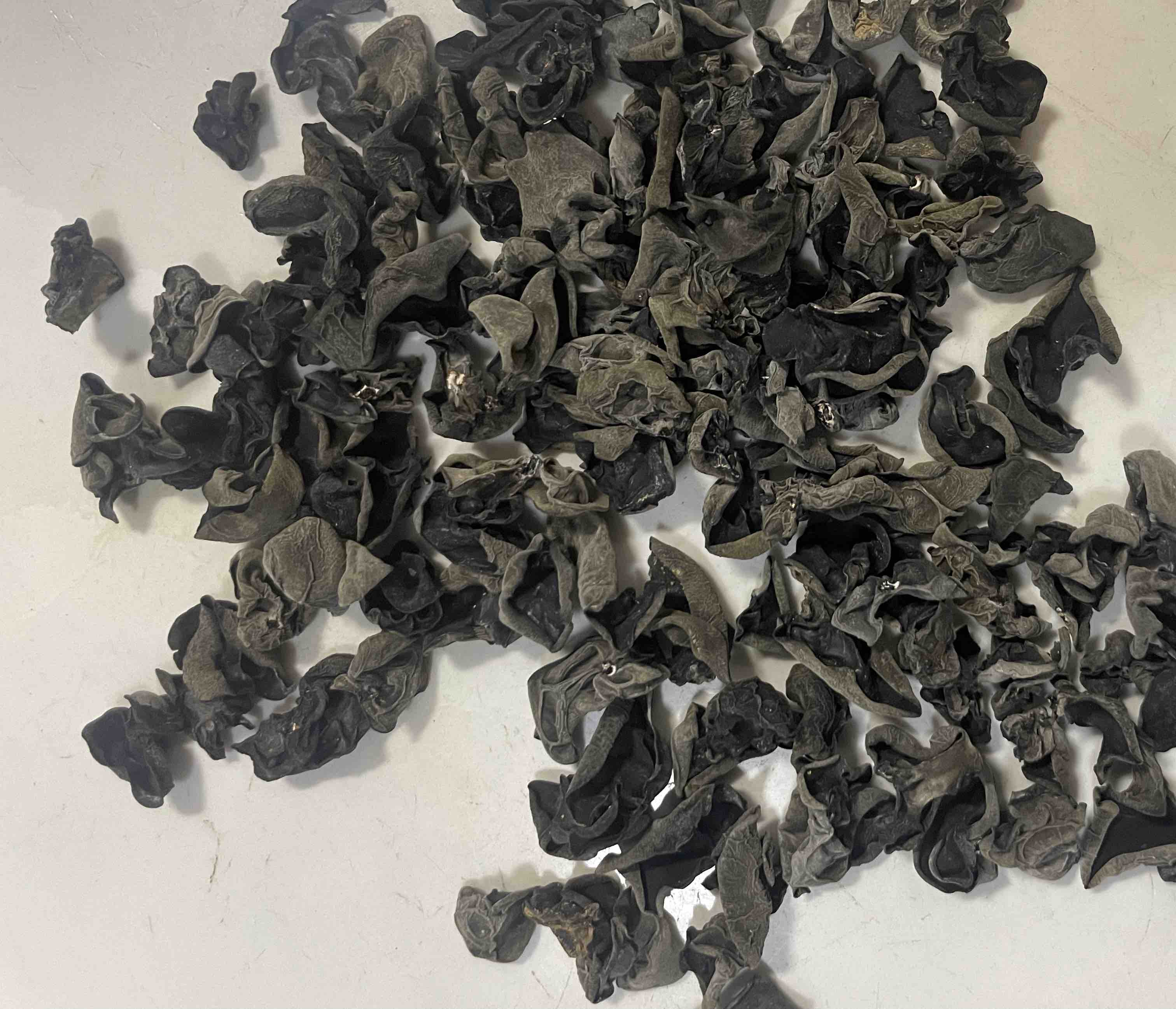 一盘散开的优质干黑木耳,呈自然卷曲状,背面灰白,正面乌黑发亮,背景为木质砧板,旁边放有一把不锈钢剪刀 干黑木耳特写