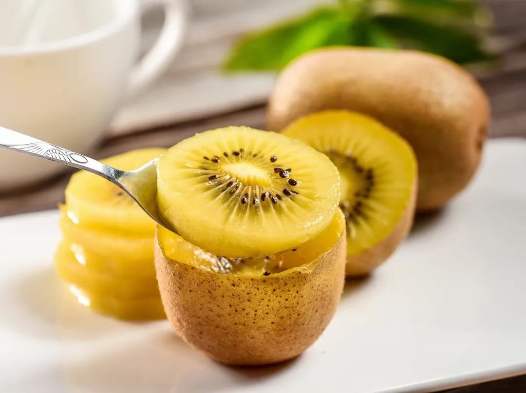 一个果盘中摆放着几颗完整的黄心猕猴桃和切片的果肉,旁边搭配其他水果,整体呈现自然清新的风格 黄心猕猴桃果盘摆盘图