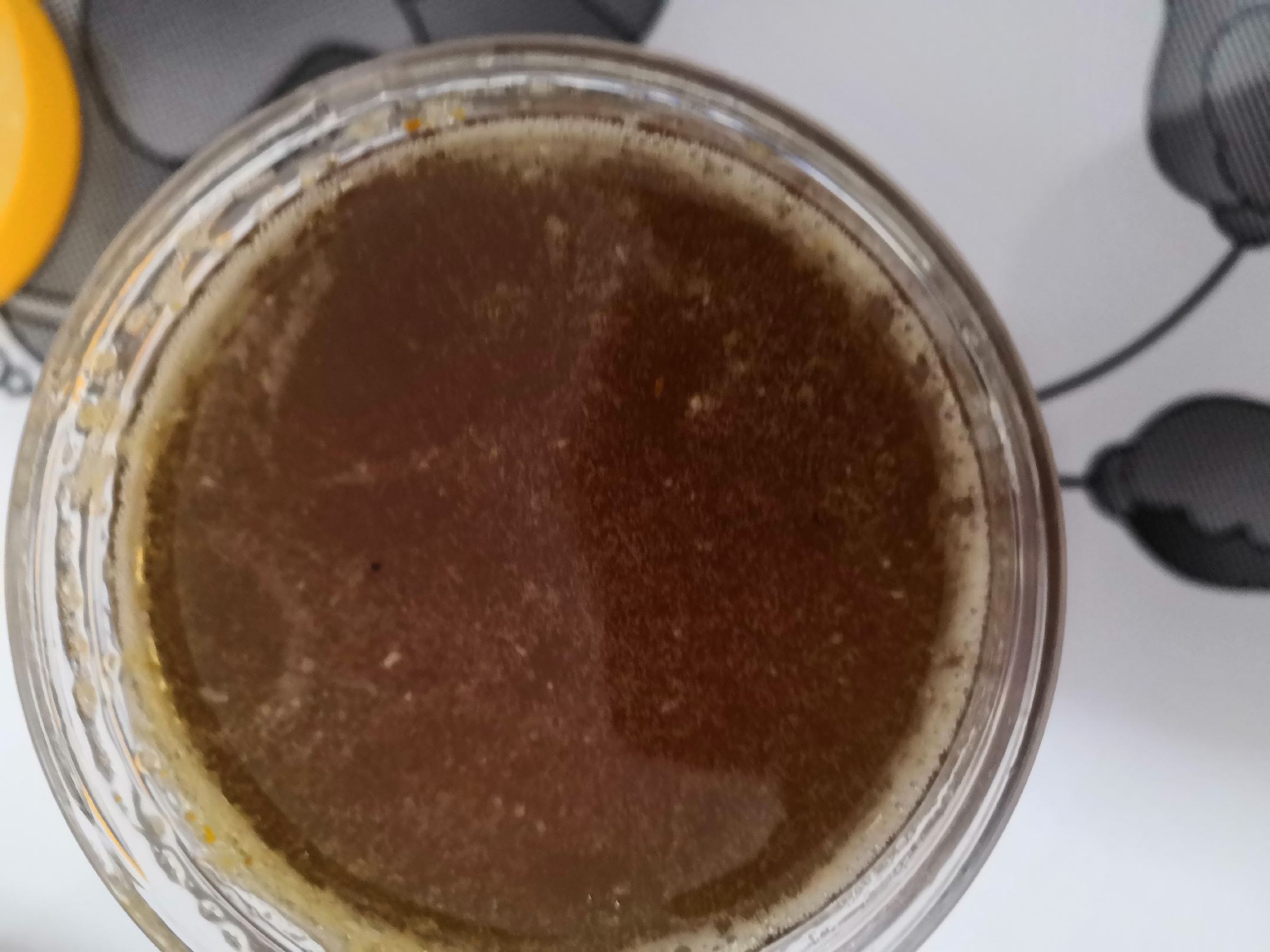 一罐透明玻璃瓶中的天然蜂蜜,呈琥珀色,质地浓稠,表面光滑反光,背景为蜂巢和盛开的槐花,展现蜂蜜的天然来源 蜂蜜特写