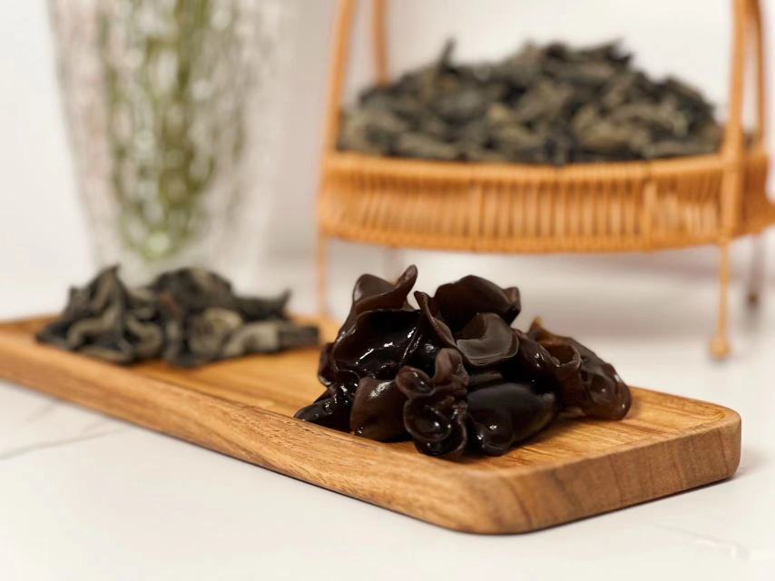 一位厨师正在炒锅中翻炒已泡发的黑木耳,旁边摆放着葱花和调料 黑木耳烹饪场景图