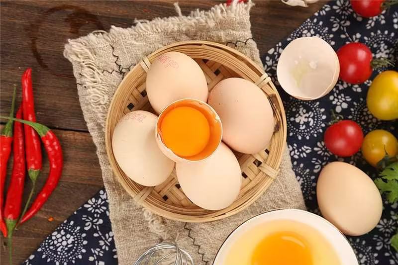 新鲜红润的西红柿与土鸡蛋并列摆放于木质砧板上，背景为厨房操作台，光线柔和自然