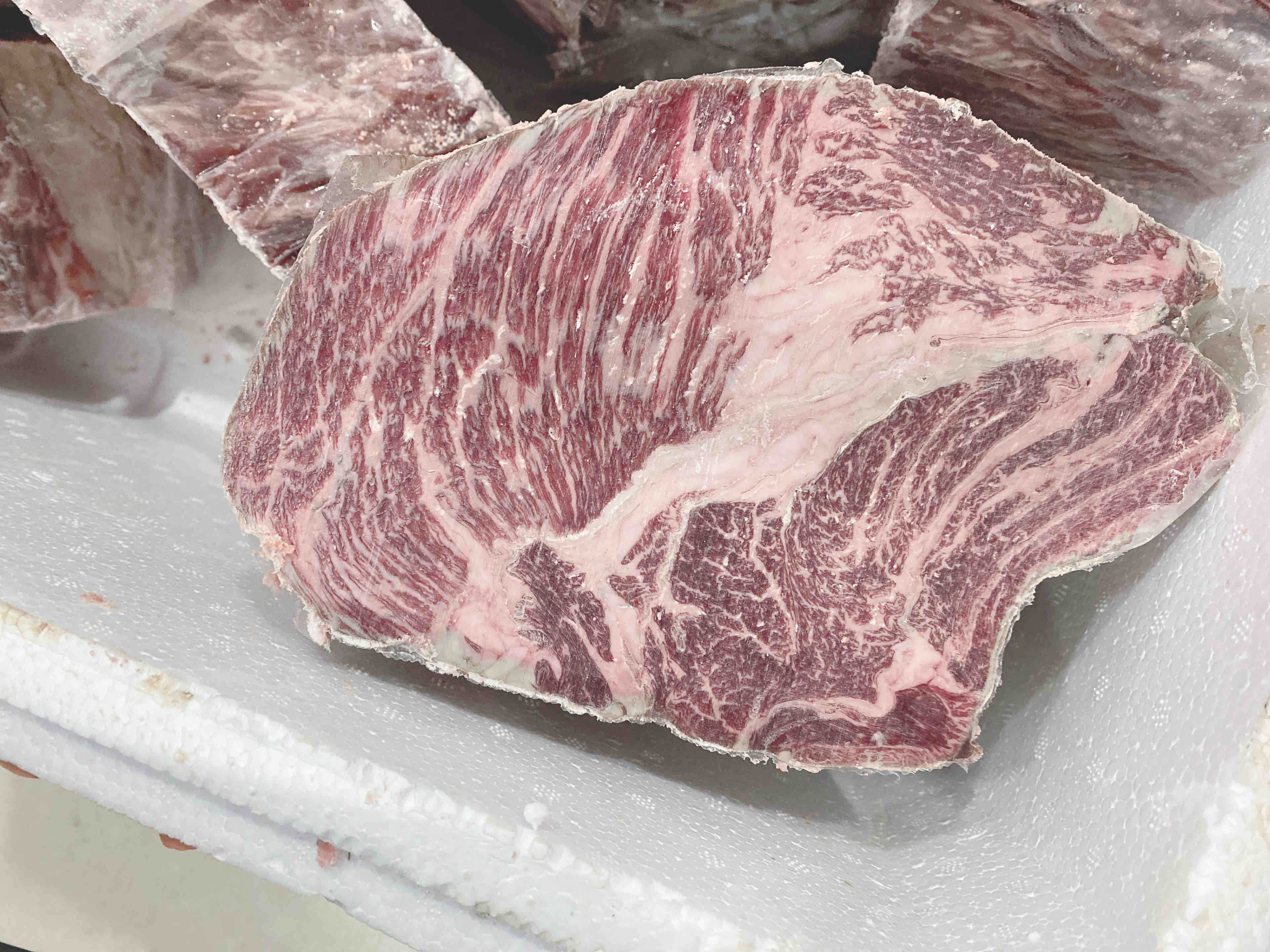 高清特写:优质牛上脑生肉块,可见清晰细腻的粉白色雪花纹理,肌肉纹理走向平行整齐,表面覆薄层天然肌膜,无注水痕迹、无淤血斑点,体现草原牛健康养殖品质 牛上脑部位特写:一块带浅粉色大理石纹的完整牛上脑肉块,表面湿润有光泽,置于竹制砧板上,旁边摆放不锈钢刀具和食品级温度计