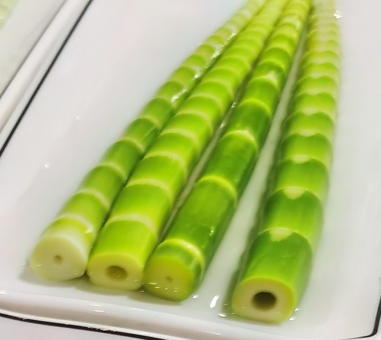 俯拍视角:不锈钢锅中清水沸腾,数根去壳后的淡绿色笋段正在焯烫,水面浮起少量白色泡沫,旁边摆放洗净的青绿笋衣与锋利厨刀,体现规范预处理流程 家庭厨房中焯水处理绿色竹笋的过程